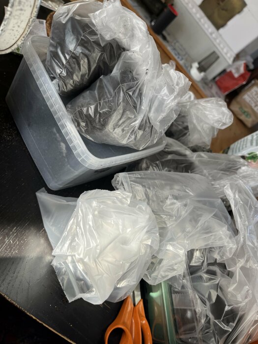 Plastförpackade föremål i behållare, sakaxel, arbetsytor, oidentifierbart innehåll, laboratorie- eller köksmiljö.