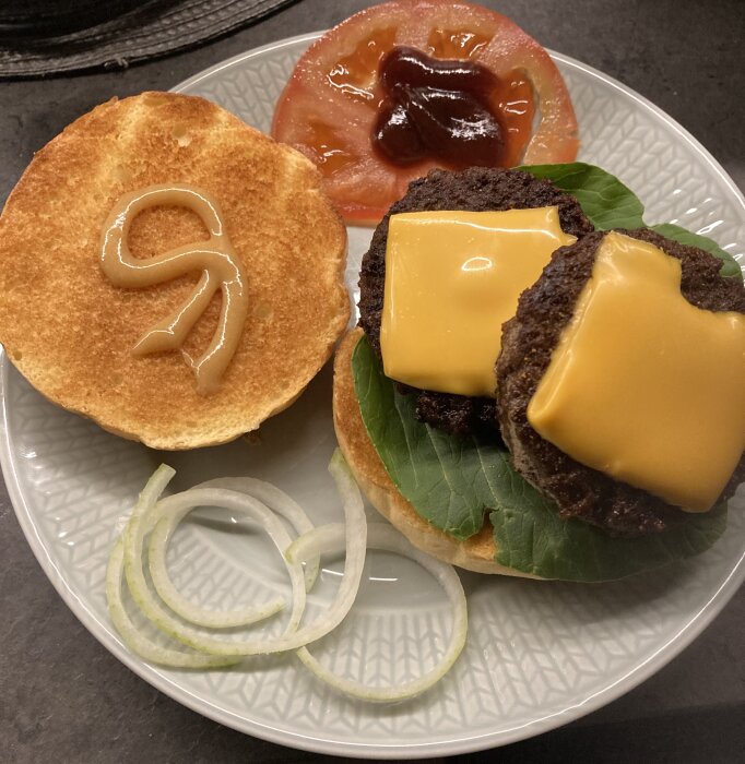 Öppen hamburgare på en tallrik med ost, lökringar, salladsblad, tomat och ketchup.