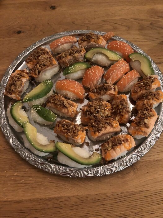 Färsk sushi med lax, avokado och krispiga löktoppingar på ett silverfat.