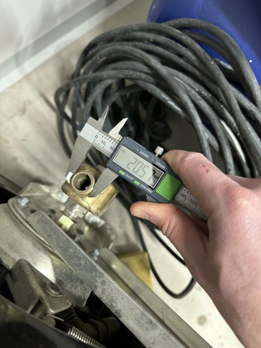 Digital skjutmått mäter komponent, visar tjugo komma sju fem millimeter, teknisk inspektion, arbetsmiljö, handverktyg.