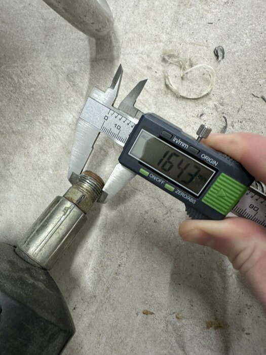 Digital skjutmått mäter en metallkomponents diameter på en arbetsbänk.