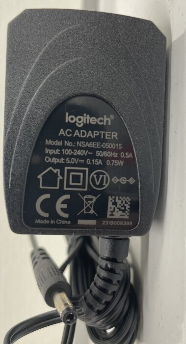 En Logitech AC-adapter med angivna input 100-240V och output 5.0V, modellnummer NSA6EE-050015, på en vit bakgrund.