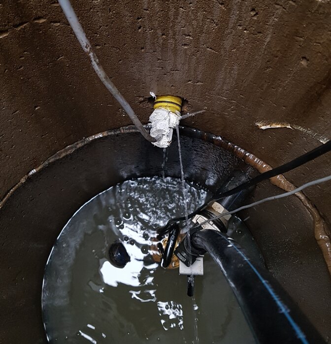 Gult kabelskyddsrör med tillfällig tätning där grundvatten läcker in i en pumpbrunn.