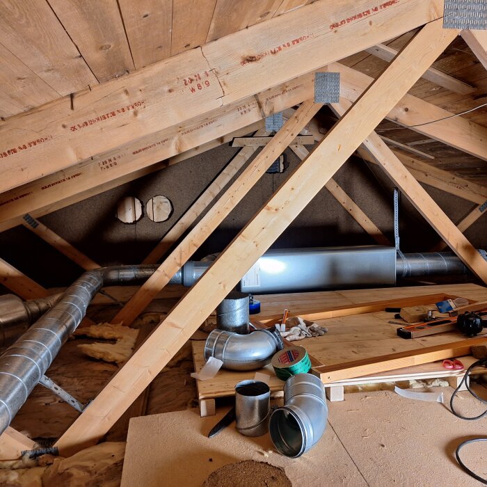 Vind med träbjälkar, isolering, byggmaterial och ventileringsrör, under konstruktion eller renovering.