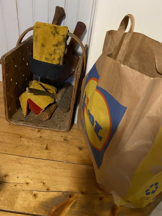 Papperskasse från Lidl bredvid en träkorg med byggverktyg och arbetshandskar.