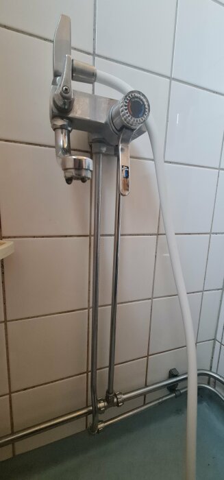 Old-fashioned single-lever bathtub mixer mounted on tiled wall, with a flexible shower hose attached.
