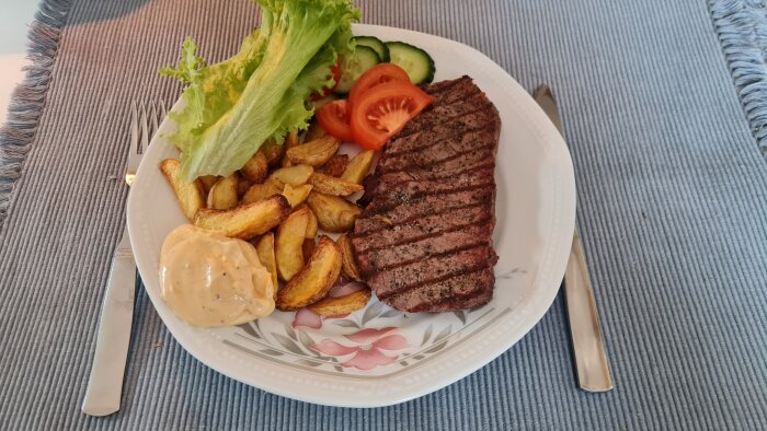 Grillad biff med kryddor, klyftpotatis, sallad, tomat, gurka och bearnaisesås på en tallrik.