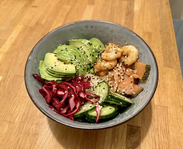 Bowl med ris, avokado, picklad rödkål, gurka, gravad lax, räkor och sesamfrön.