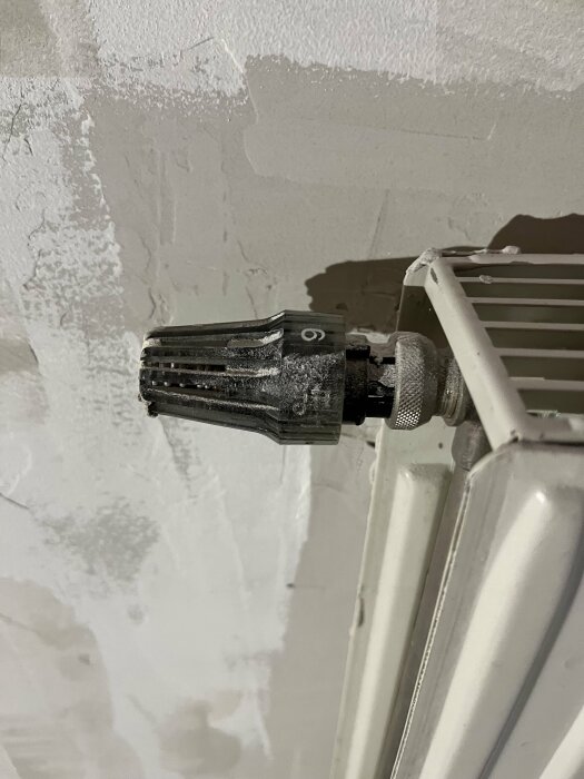 Termostat på radiator, vit vägg med ojämn spackling, renoveringsarbete antyder pågående arbete eller reparation.