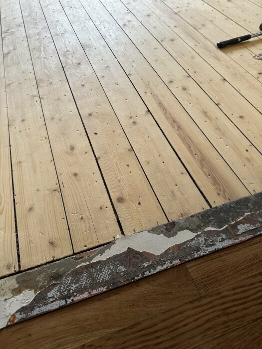 Trägolv under renovering, verktyg på golvet, gammal färg på betonggrund synlig.