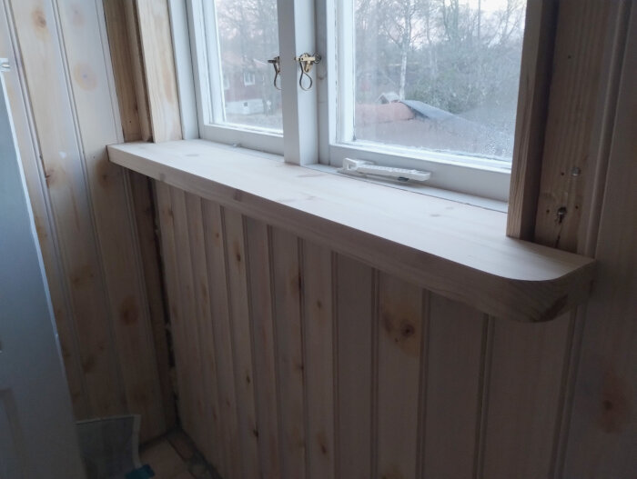Nyinstallerad träfönsterbänk i ett renoverat rum med träpanelväggar.
