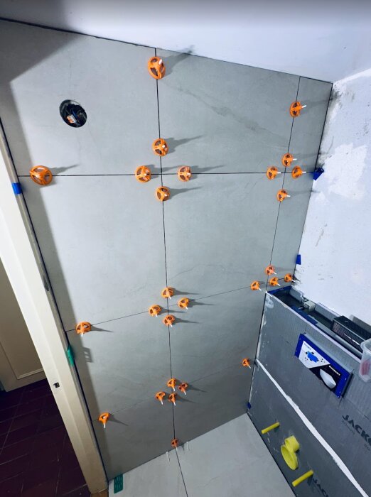 Gråa kakelplattor på vägg med distanser och nivelleringssystem under installation i badrum.