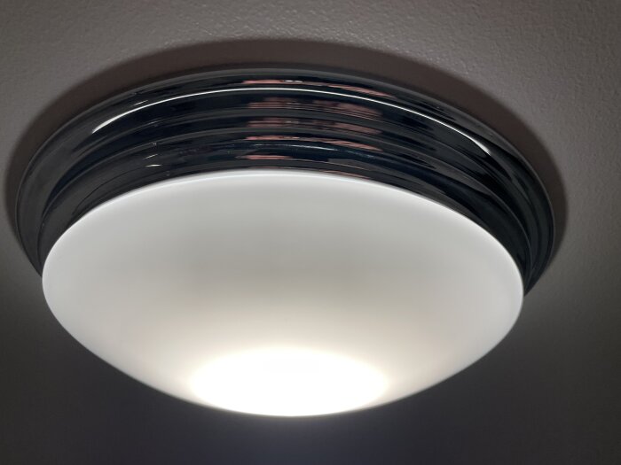 Takmonterad plafond med kromkant och vit diffusor som lyser.