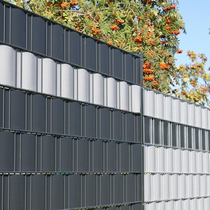 Modernt staket, metalliska lameller, bakom växt med orange bär, klar himmel.
