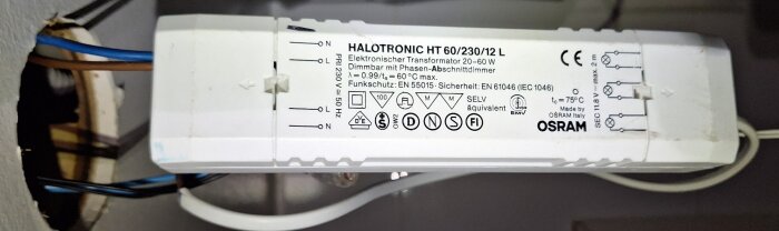 Elektronisk transformator för halogenlampor, märkt med tekniska specifikationer och säkerhetsstandarder, installerad med kablar.