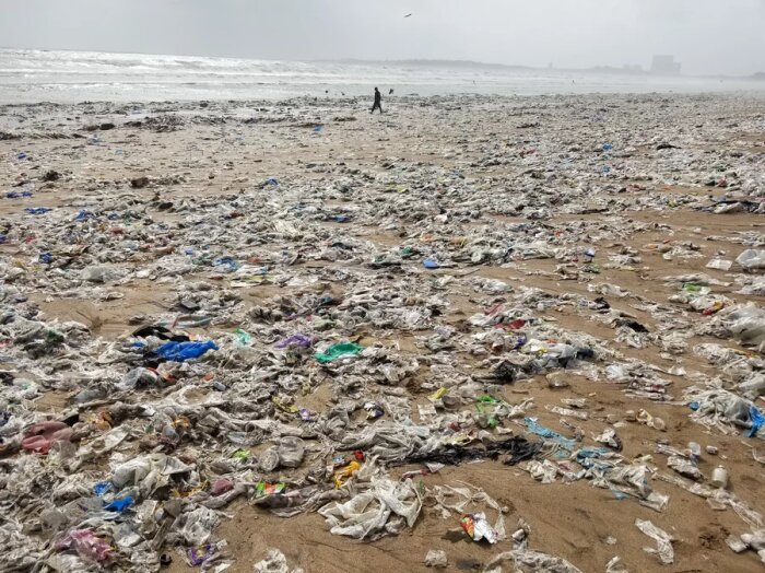 Strandöversållad med plastskräp och avfall, person i bakgrunden, miljöförstöring på Juhu Beach.