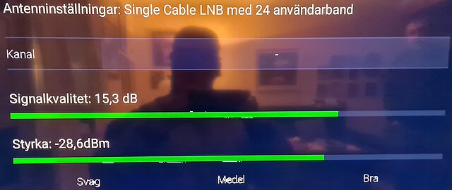 Reflexion av person framför TV-skärm som visar signalstyrka och kvalitet för antenninställningar.