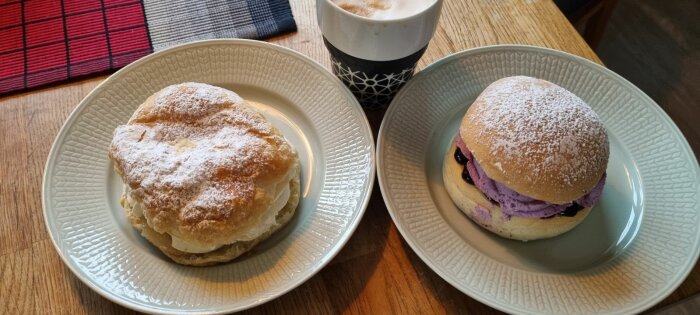 Två olika semlor på fat bredvid en kopp kaffe, en traditionell och en med lila fyllning.