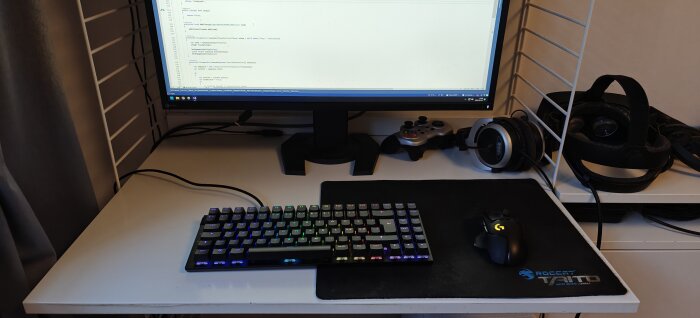 Ergonomisk TKL-tangentbord med bakgrundsbelysning på skrivbord bredvid datormus och hörlurar.