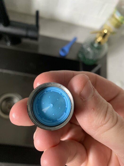 Person som håller ett vattenkranfilter visande den blå silen och gängan.