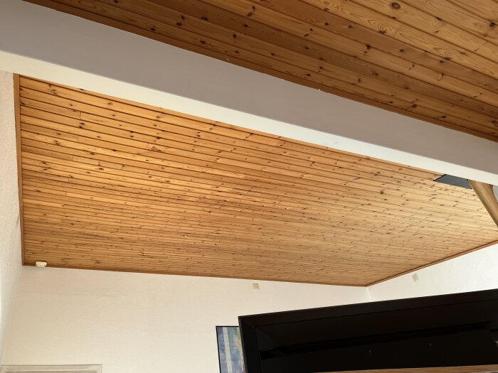 Innertak med träpanel och synlig buktning längs väggkanten, inga lös paneler synliga.
