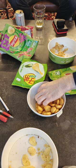 Blindtest av olika asiatiska chips på ett bord med öppnade påsar och en hand som tar chips.