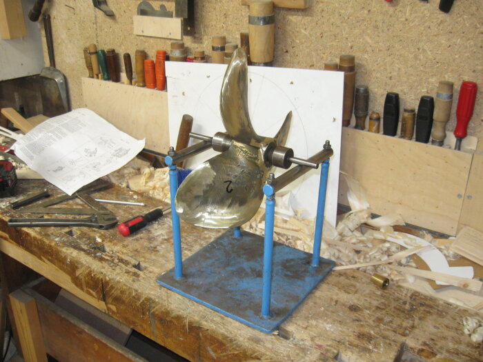 Balanserad propeller på en blå balanseringsapparat i en verkstad full av verktyg och träspån.