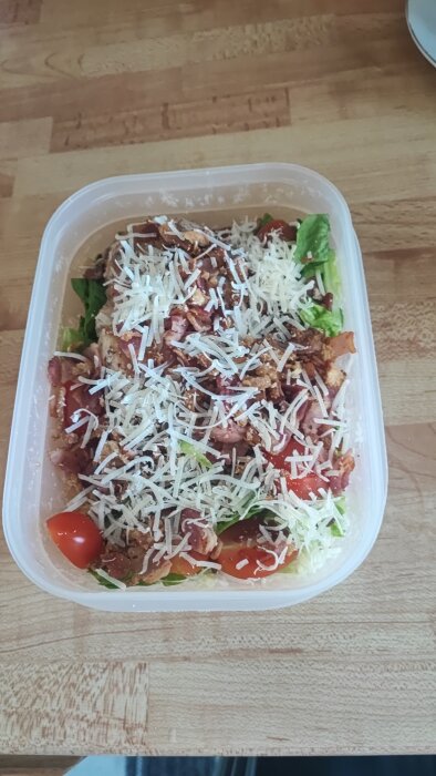 Ceasarsallad med extra rostad lök och riven parmesan i en matlåda, placerad på ett träbord.