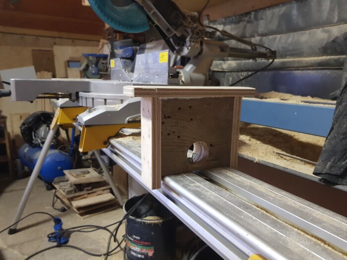 Hemmagjord trästöd monterad på sågbord i en verkstad full av verktyg och träspill.