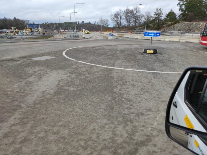 Bild tagen från bil som visar en tom rondell med vägmarkeringar och skyltar under dagsljus.
