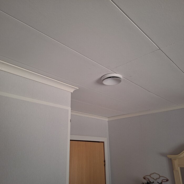 Ventilationsdon i taket i ett sovrum, med en synlig dörr och en del av en säng.