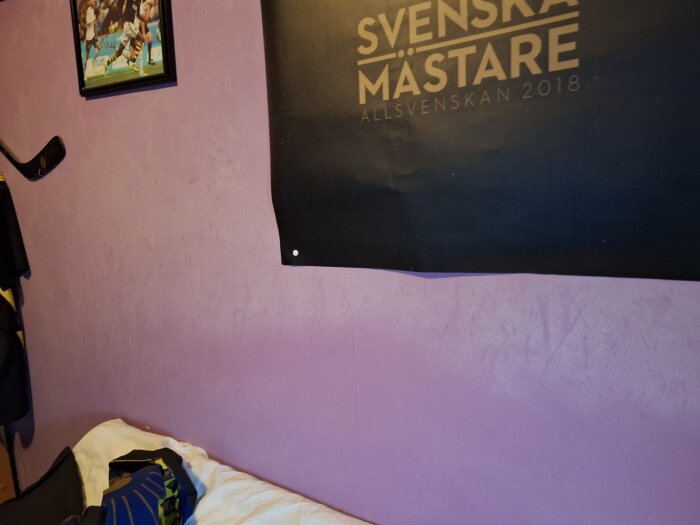 Vit beläggning på en lila betongvägg i ett sovrum vid sängen, med poster och hockeyklubba.