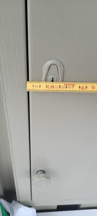 Måttband som mäter avståndet mellan dörr och dörrhandtag för att bestämma skruvlängd.