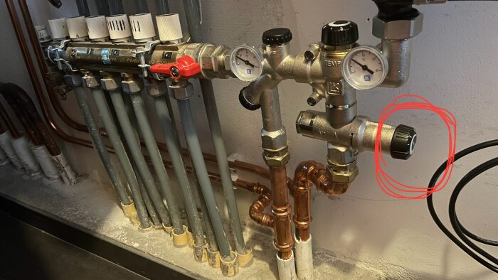 Inringad svart ratt på värmesystems kopplingar med rör och manometrar i ett pannrum.