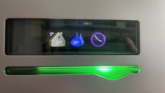 Display på värmepump med ikoner för hus, vattendroppar och klocka, visande 20°C och 28°C.
