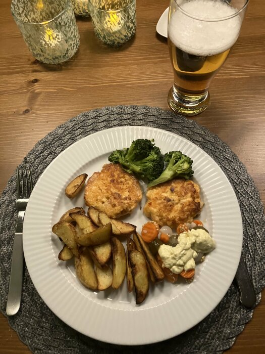 Laxburgare med potatisklyftor, broccoli och remouladsås på tallrik, bredvid ett glas alkoholfri öl.