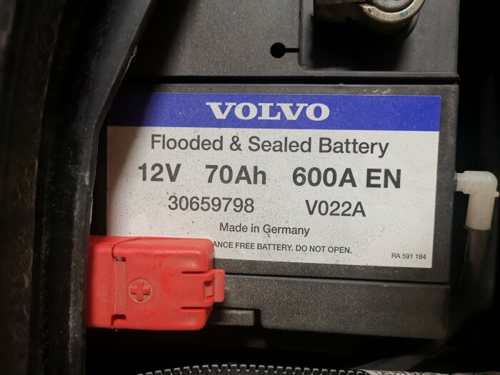 Etikett på bilbatteri som visar "Flooded & Sealed Battery 12V 70Ah 600A" i en Volvo V70.