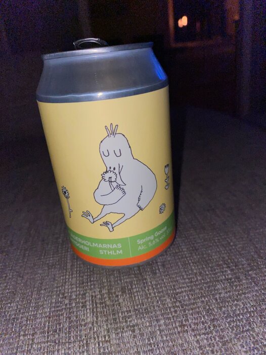 Burk öl av typen Brown Ale med illustration på etiketten, står på ett bord i dunkelt ljus.