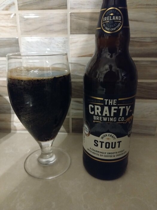 Ölglas fyllt med stout och en flaska från The Crafty Brewing Co. på ett bord.