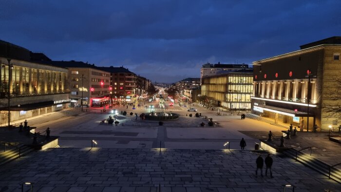 Vy över upplyst stadsgata vid skymning med byggnaden Konserthuset till vänster och människor.