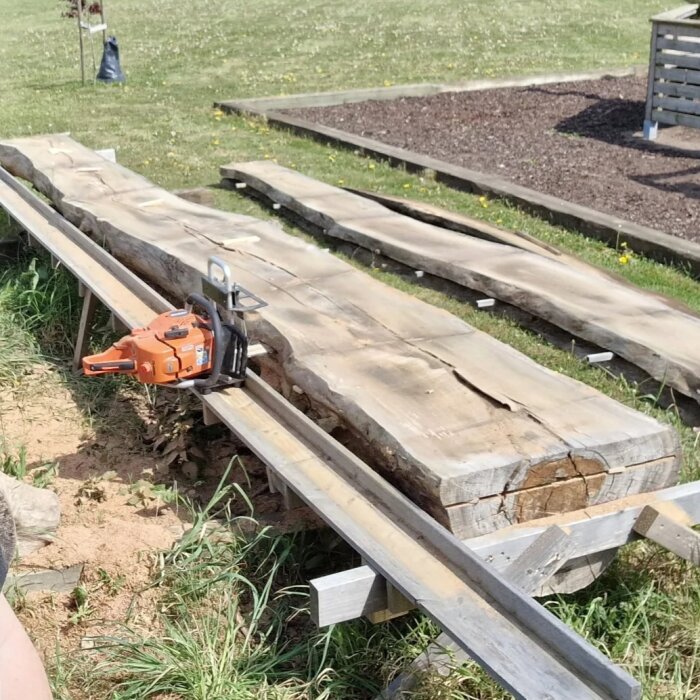 Motorsåg monterad på ett sågverk för att klyva en okantad trädplanka utomhus.