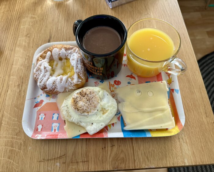 Frukostbricka med stekt ägg, ostsmörgås, wienerbröd, varm choklad och apelsinjuice.