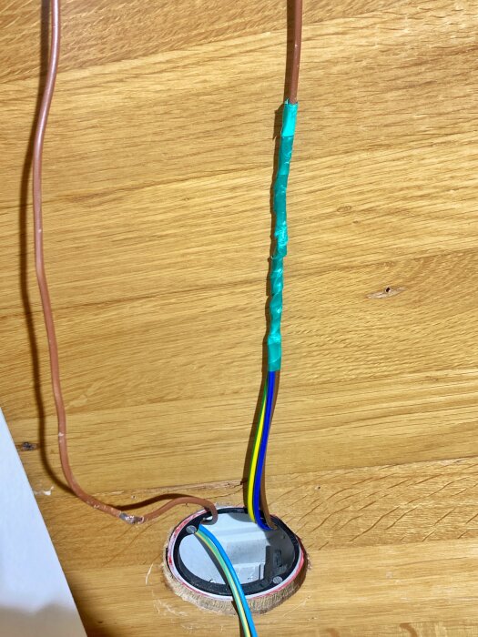 Nyinstallerade kablar och vägguttag i dosa med tejpade och färgkodade ledningar på träyta.
