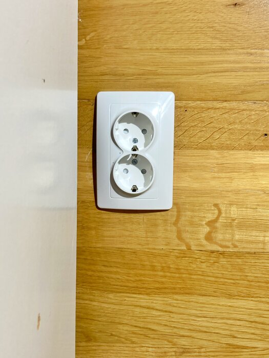 Nytt dubbelvägguttag monterat på träpanelvägg vid kanten av en vit vägg.
