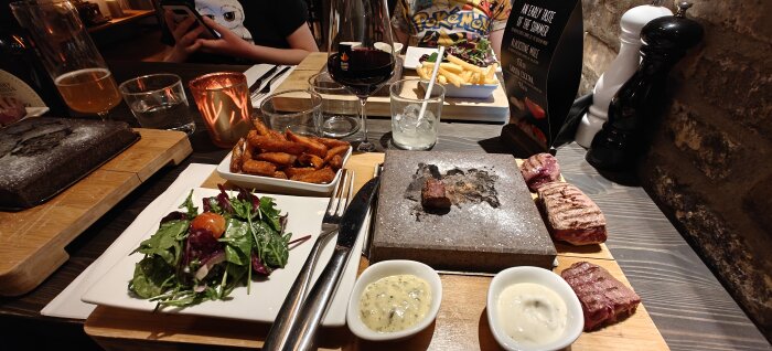 Middagsbord med kött på het sten, sallad, sötpotatispommes, såser, vin och öl.