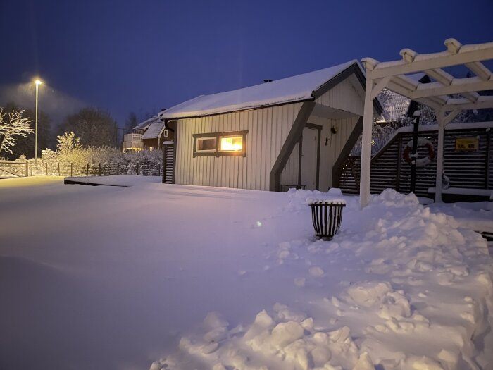 Ett hus med snötäckt tak och trädgård under kvällsljus.