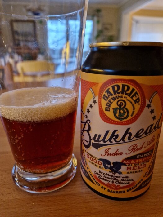 Burk med Bulkhead India Red Ale bredvid ett delvis fyllt ölglas på ett bord.