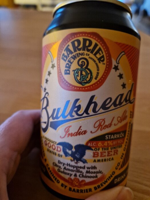 Hand håller en ölburk märkt "Bulkhead India Red Ale" från Barrier Brewing Co., färgglad med örnmotiv.