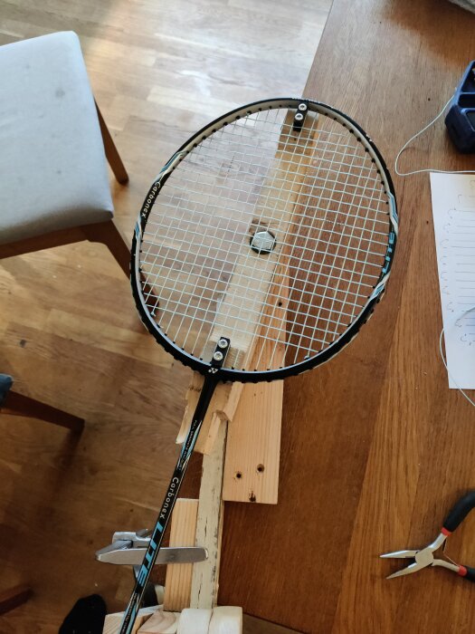 Hembuilt omsträngningsjigg med ett badmintonracket fastspänt på en hemmagjord träplattform med spännanordning och kullager.