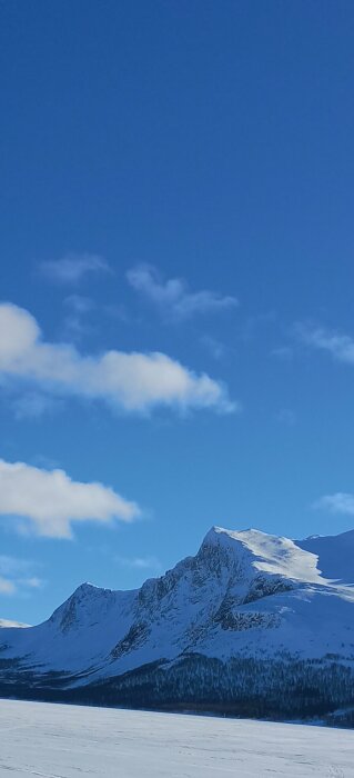 Snötäckt bergstopp mot en klarblå himmel med vita moln.